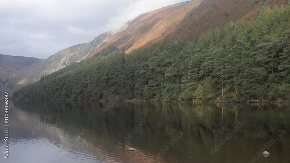 Serene lake surrounded by pine trees and misty hills in Glendalough, Ireland during a cloudy day Serene lake surrounded by pine trees and misty hills in Glendalough, Ireland during a cloudy day