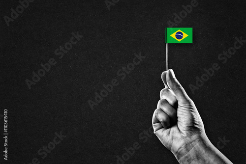 Hand in Black and White Holding Brazil Flag, Black Textured Background with Copy Space photo