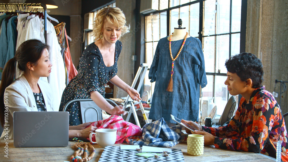 Three Female Fashion Designers In Studio Meeting Discussing Garment On Dummy Three Female Fashion Designers In Studio Meeting Discussing Garment On Dummy