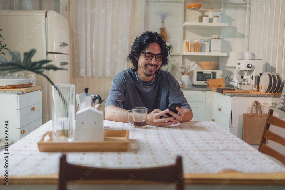 Smiling Man Using Smartphone at Cozy Kitchen Table in Bright, Vintage-Style Home Smiling Man Using Smartphone at Cozy Kitchen Table in Bright, Vintage-Style Home