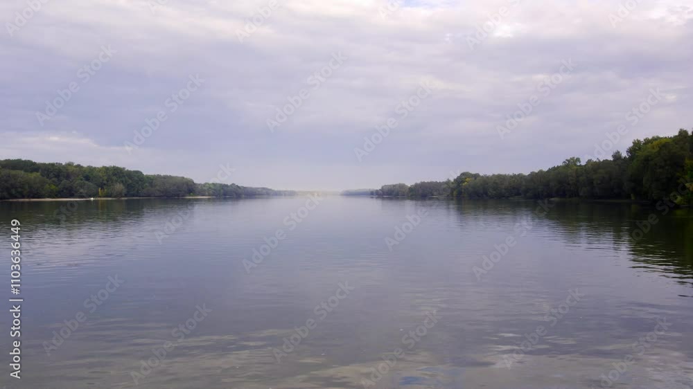 Serene river flows through lush green landscape on a cloudy day in autumn Serene river flows through lush green landscape on a cloudy day in autumn