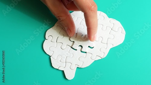 Close-up of a hand placing a missing puzzle piece into a brain shape on a teal background, illustrating cognitive engagement and problem-solving.