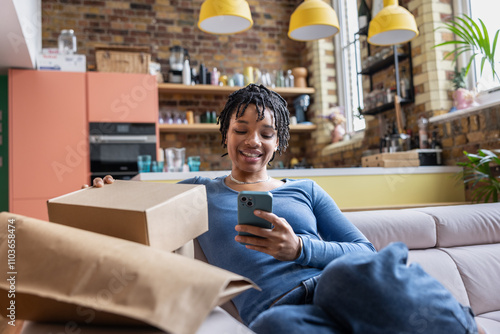 Happy young female entrepreneur looking at order details from e-commerce site and stacking parcels to ship photo