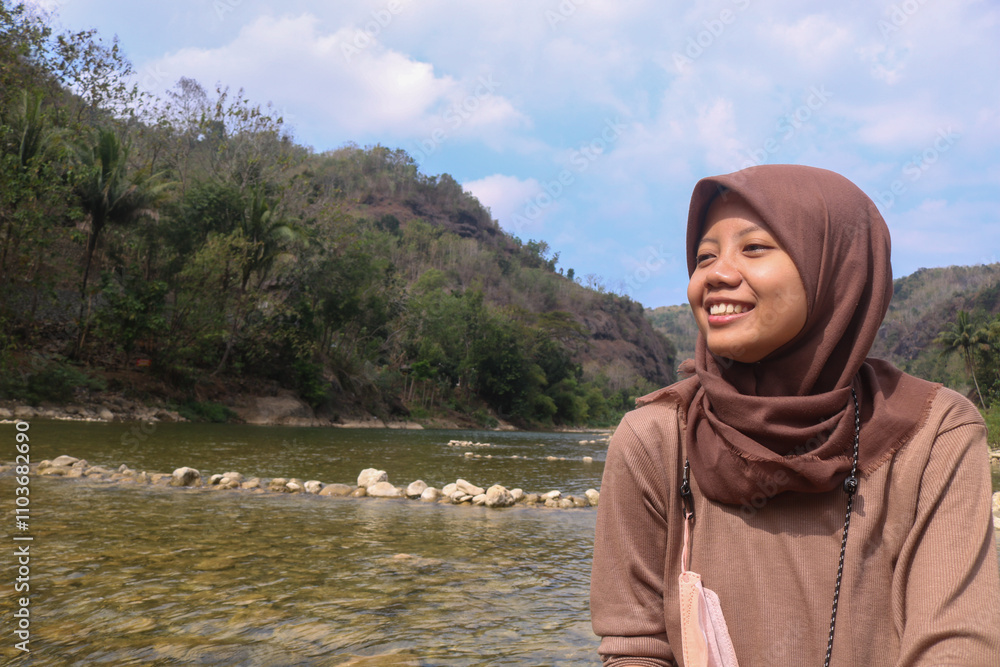 A girl sitting on a river rock smiling. Grounding in the river enjoying the natural scenery A girl sitting on a river rock smiling. Grounding in the river enjoying the natural scenery