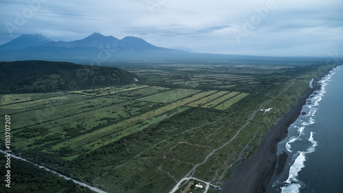 Aerial view of Khalaktyrsky Beach. A tranquil scene with a black sand beach, gentle waves, and lush mountains under a cloudy sky for a perfect getaway photo