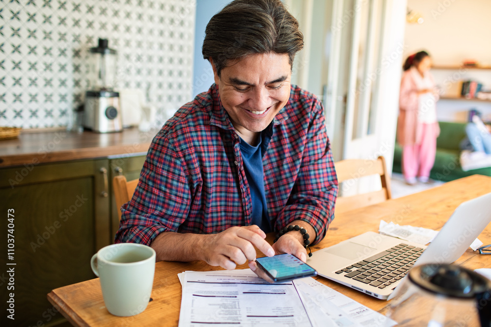 Stressed man looking at laptop with bills on tablet at kitchen Stressed man looking at laptop with bills on tablet at kitchen