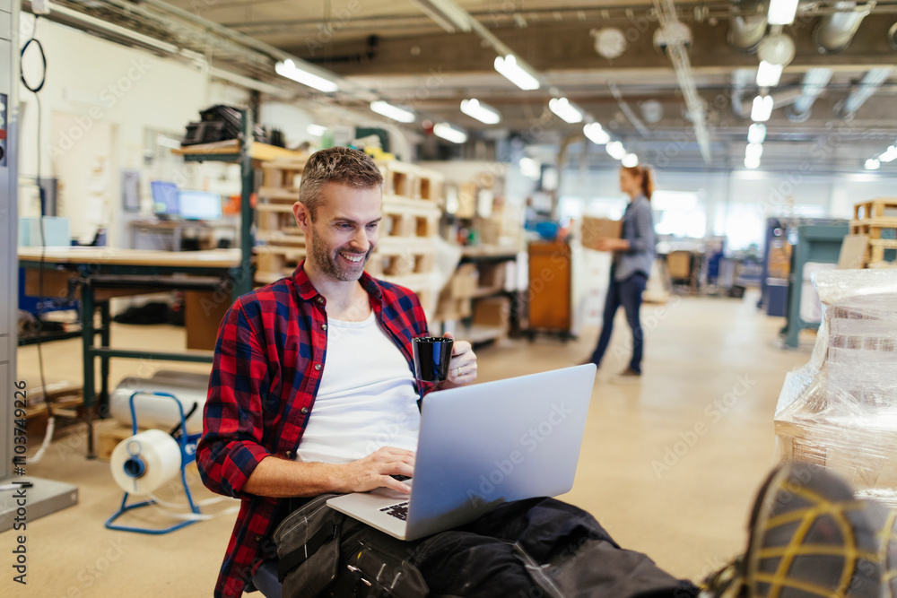 Fototapeta premium Young man using a laptop while working in a printing press office