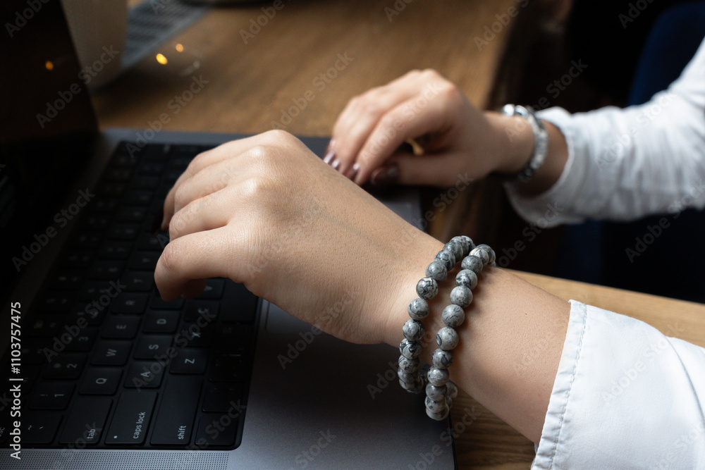 Obraz premium Hands of a young unrecognizable girl in a white shirt with bracelets typing on a laptop keyboard. Close-up. View from above. Hands of an office worker. High quality photo