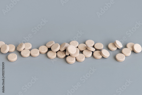 Pile of beige herbal pills in a line on grey close up. Taking dietary supplements and vitamin