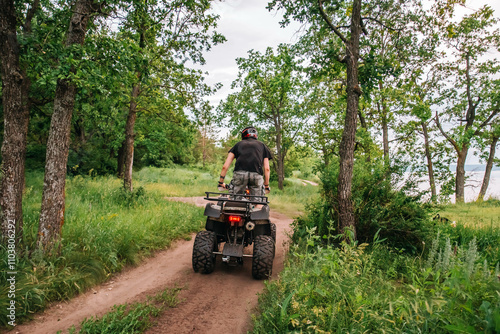 a girl and a guy bikers ride quad bikes in a beautiful green forest on a river cliff, their dogs are running nearby