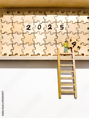 A small figure on a ladder is placing the final puzzle piece, completing the year "2025" on a wooden puzzle board. new year change concept.