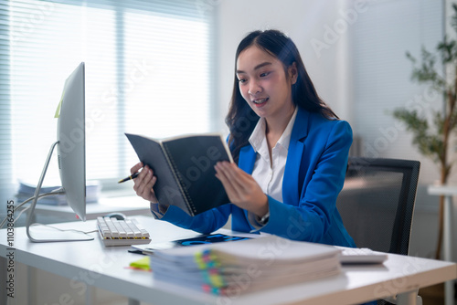 A woman in a blue suit is reading a book at her desk