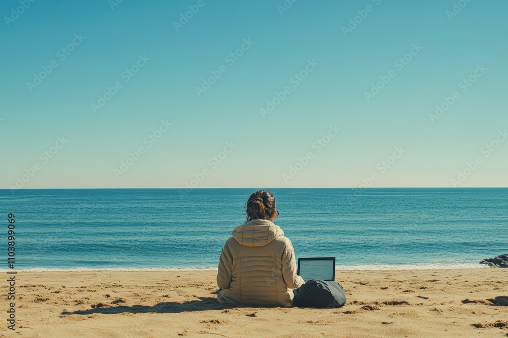 A person sitting on the sand using a laptop while facing the open ocean under a clear sky A person sitting on the sand using a laptop while facing the open ocean under a clear sky