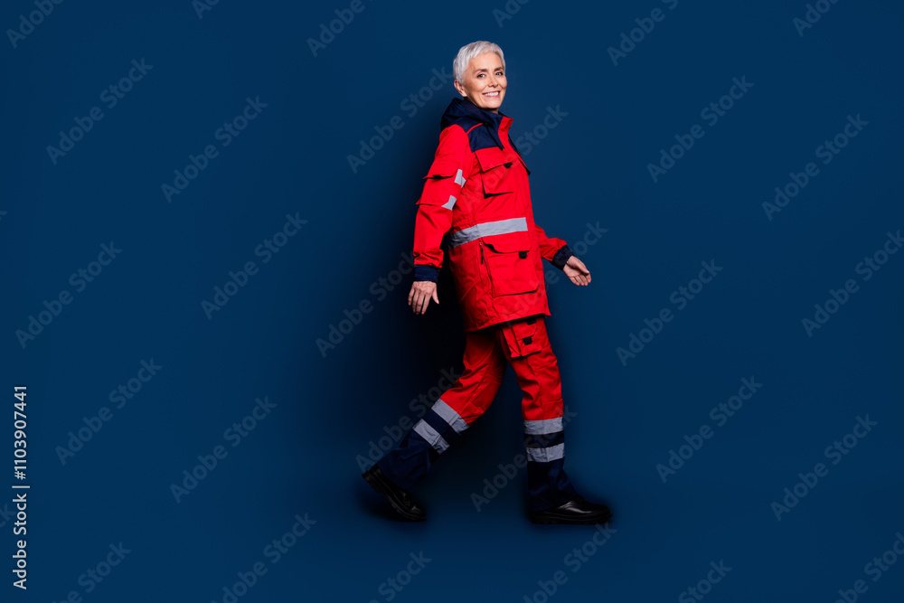 Full size photo of attractive mature lady profile walking wear uniform paramedic doc insurance assistance isolated on dark blue background Full size photo of attractive mature lady profile walking wear uniform paramedic doc insurance assistance isolated on dark blue background