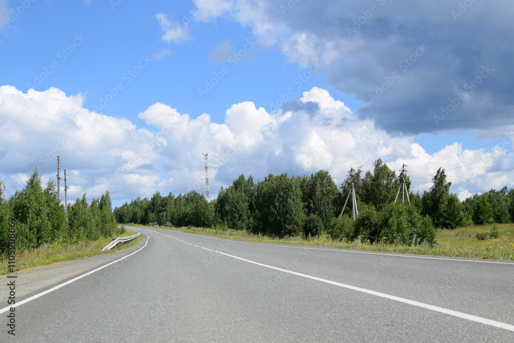 Fototapeta premium Empty highway surrounded by forest. Beautiful summer landscape, white clouds on a blue sky.