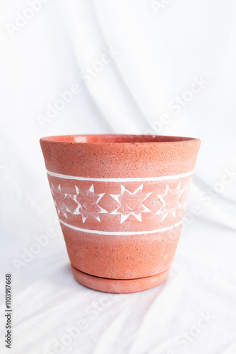 Close-up of a terracotta flower pot with a white 8-pointed star pattern, showcasing the textured finish and earthy tones