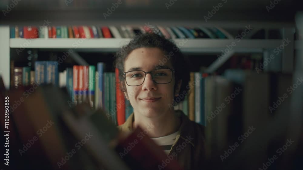 Young gen Z student wearing glasses standing behind bookshelf in college library, looking into camera with smile. Video portrait Young gen Z student wearing glasses standing behind bookshelf in college library, looking into camera with smile. Video portrait