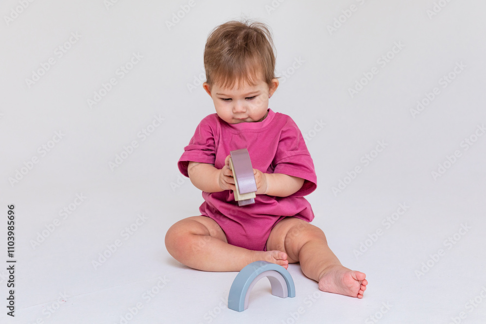 Cute baby little girl in pink bodysuit playing with colorful rainbow toy pyramid sitting on floor. Child with educational toy. Early development, white background. copy space. High quality photo Cute baby little girl in pink bodysuit playing with colorful rainbow toy pyramid sitting on floor. Child with educational toy. Early development, white background. copy space. High quality photo