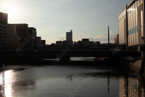 This beautiful city scene was taken in Hiroshima. The sun is starting to set showing a dimly lit orangey hue. The canal that runs through is seen with bridges crossing over for pedestrians or cars. photo