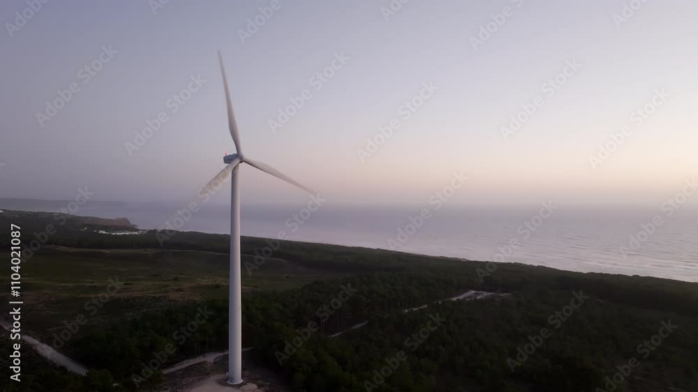 Wind turbine rotates gracefully near the ocean, creating a serene scene at sunset with vibrant colors in the sky Wind turbine rotates gracefully near the ocean, creating a serene scene at sunset with vibrant colors in the sky