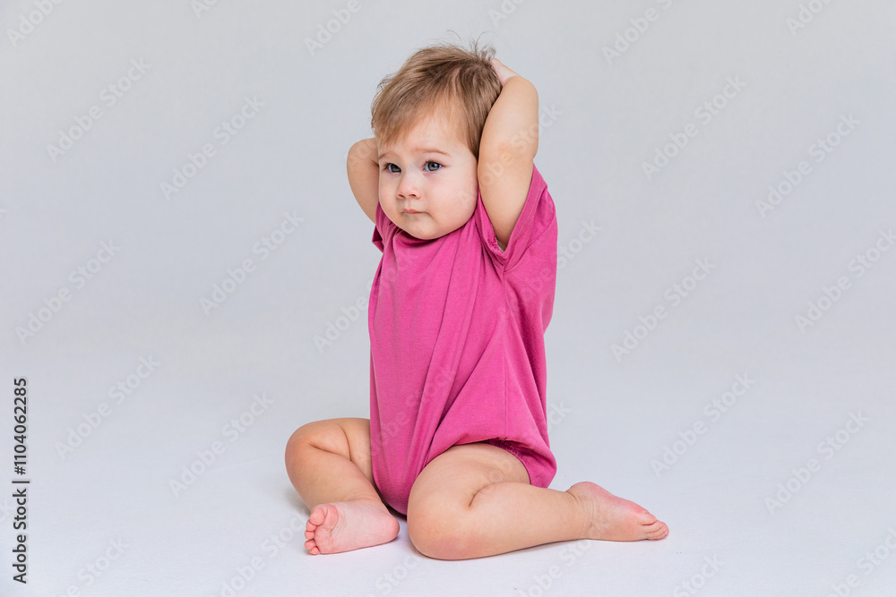 Cute baby girl in a pink bodysuit sitting on a white background with empty copy space. Closeup. Childhood and fashion. Birthday party concept. High quality photo Cute baby girl in a pink bodysuit sitting on a white background with empty copy space. Closeup. Childhood and fashion. Birthday party concept. High quality photo