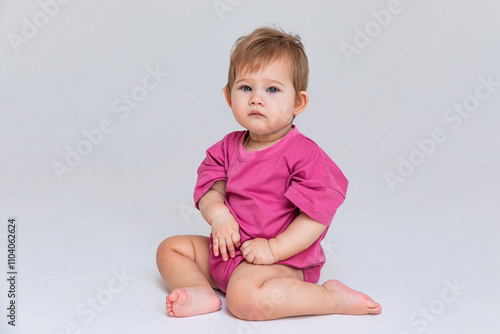 Cute baby girl in a pink bodysuit sitting on a white background with empty copy space. Closeup. Childhood and fashion. Birthday party concept. High quality photo