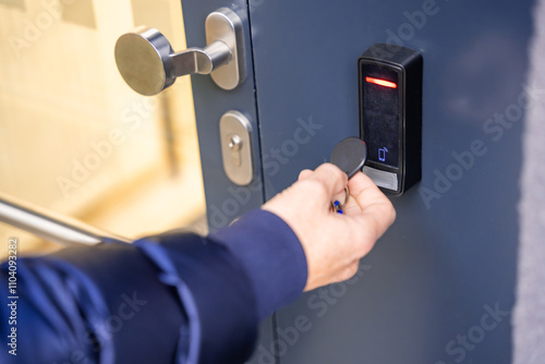 Close up view of person using a electric lock key fob to access a building via a reader of entry system mounted on a house wall photo