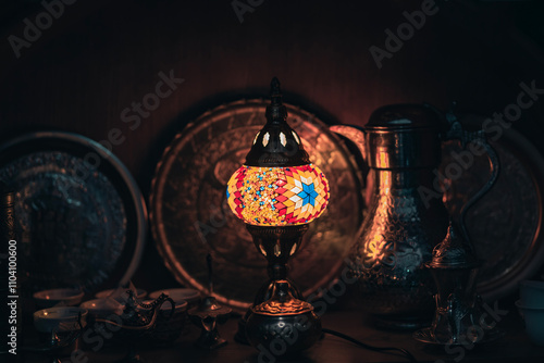 Tableau sur toile A traditional Turkish mosaic lamp with colorful glass details illuminates metal dishes and decorative items, creating a warm, mystical atmosphere