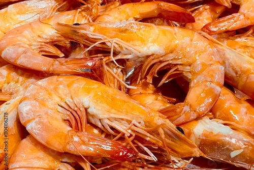 Cooked shrimp, which should be steamed or boiled. Ready-to-eat food, as can be identified by the bright orange shell and shiny appearance. The shrimp are arranged closely together.