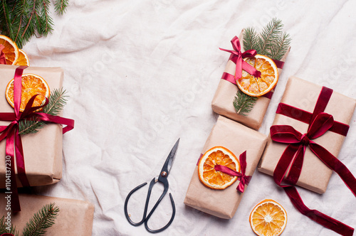 Wrapped gifts with dried orange and velvet pine branches and bows on white linen Christmas decoration diy recipe copy space flat lay top view holiday inspiration