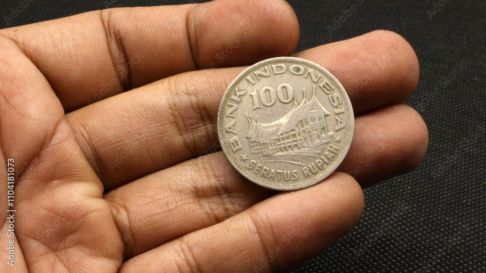 Hand holding an old coin of one hundred rupiah Hand holding an old coin of one hundred rupiah
