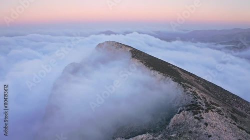 Dramatic aerial perspective of mountain peaks covered in fog and clouds during a vibrant sunset, with breathtaking twilight colors in the sky.