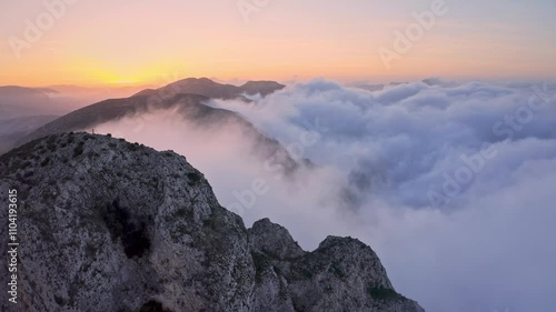 Flying above misty mountain peaks during a vivid sunset, capturing the ethereal beauty of nature with glowing skies and serene fog layers.