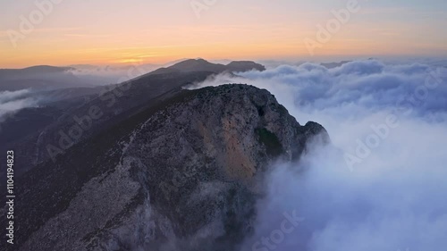 Epic aerial drone view of majestic mountains shrouded in clouds and fog at sunset, showcasing vibrant twilight colors and dramatic scenery.