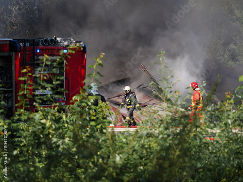 Walking firefighter against smoke environments during day time and burning building.