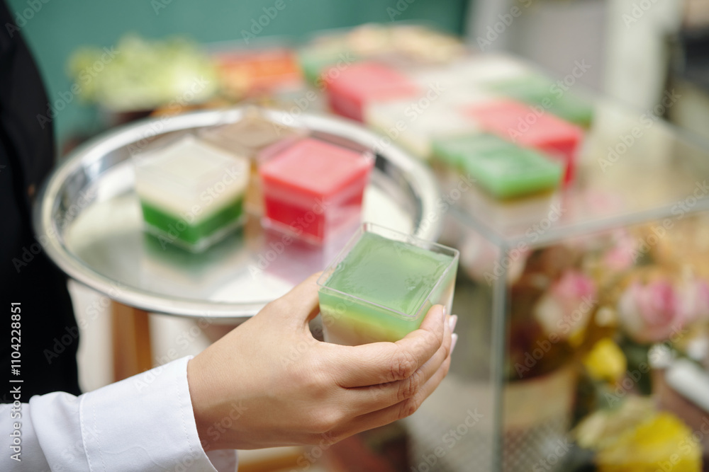 Hand holding tray with colorful cubes, possibly soap or jelly, in a market or shop. Bright colors and background with floral arrangements adding vibrant feel Hand holding tray with colorful cubes, possibly soap or jelly, in a market or shop. Bright colors and background with floral arrangements adding vibrant feel