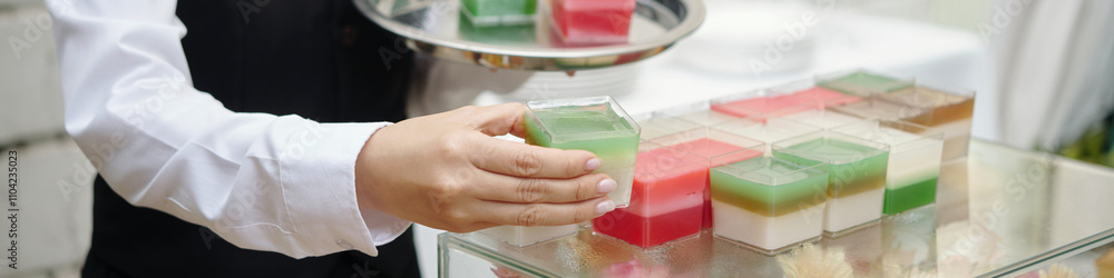 Hand of server in white shirt presenting assorted colorful dessert dishes on a tray during a formal event or celebration creating an elegant ambiance Hand of server in white shirt presenting assorted colorful dessert dishes on a tray during a formal event or celebration creating an elegant ambiance