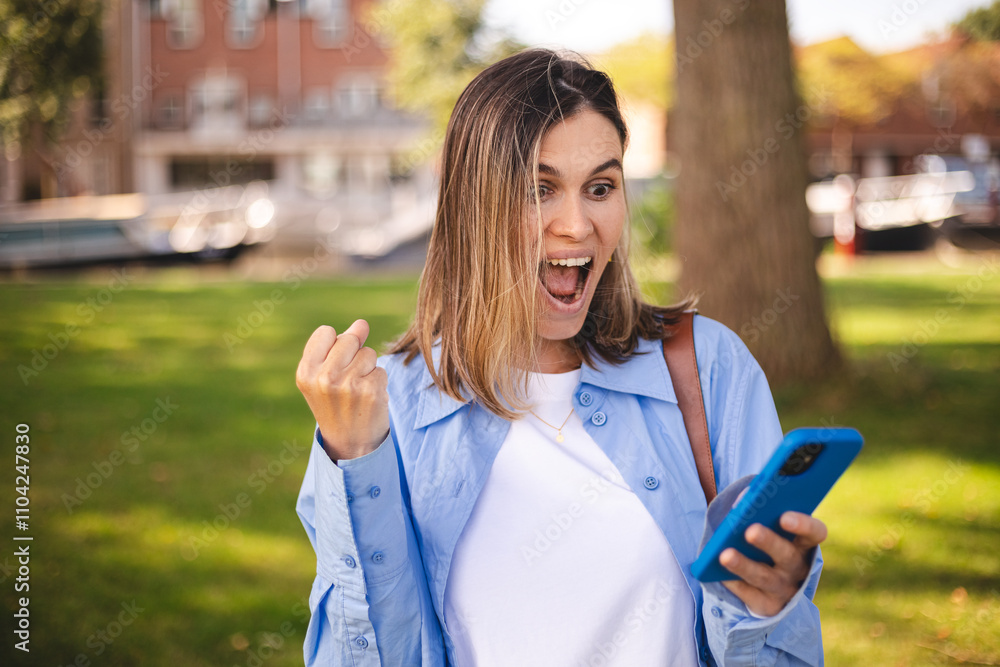 Blonde short hair woman browsing internet with cellphone mobile phone wearing casual clothes shirt gesturing like winner. Smiling open mouth woman look happy, celebrating win, triumph, success, wow. Blonde short hair woman browsing internet with cellphone mobile phone wearing casual clothes shirt gesturing like winner. Smiling open mouth woman look happy, celebrating win, triumph, success, wow.