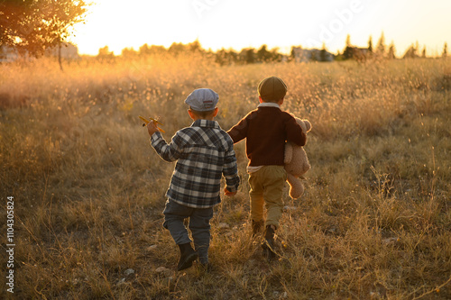 A young boys wearing a cap holding a plush teddy bear, standing in a field at sunset. The warm, golden light creates a nostalgic and peaceful atmosphere. Ideal for themes of childhood, innocence photo