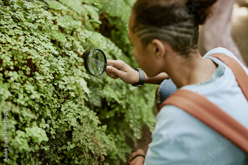 High angle over shoulder shot of curious teen Black boy looking closer at maidenhair fern using magnifying glass