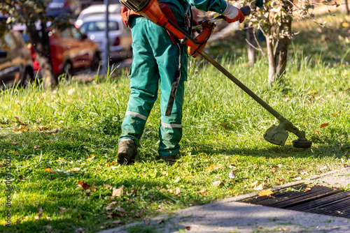 Slika na platnu Landscape maintenance worker trimming grass in urban park during autumn afternoo