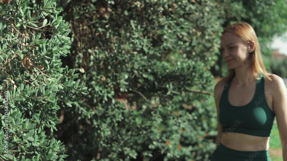 Young sportswoman enjoying stroll in park, taking moment to smell vibrant flowers blooming in bush, embracing beauty of nature and healthy lifestyle Young sportswoman enjoying stroll in park, taking moment to smell vibrant flowers blooming in bush, embracing beauty of nature and healthy lifestyle