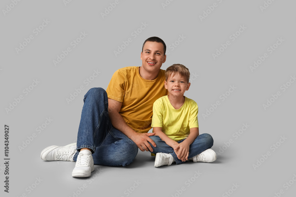 Happy father and his little son sitting on grey background Happy father and his little son sitting on grey background