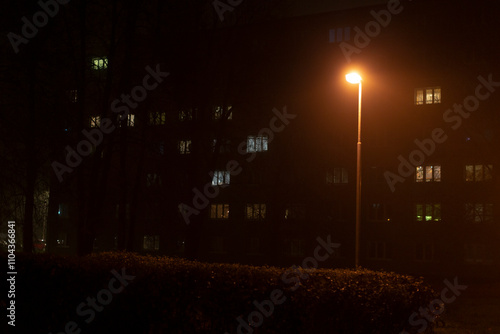 In a fogladen urban scene, a solitary street light casts a gentle glow on a nearby residential building, contributing to the tranquil, serene, and enigmatic ambiance of the peaceful, quiet night photo