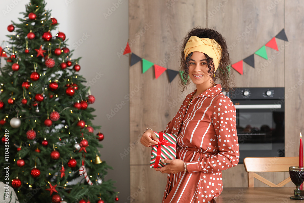 Fototapeta premium Young African-American woman with gift box celebrating Kwanzaa in kitchen