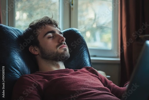 Tranquil Young Man Lost in Thought, Relaxing in a Cozy Armchair with His Computer