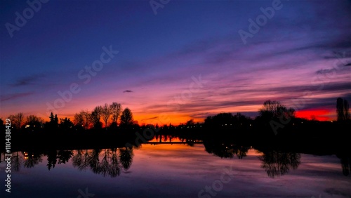 Colorful sunset above the lake with trees silhoutes