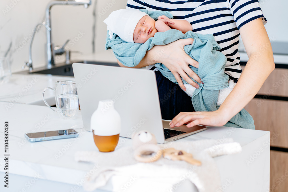 Fototapeta premium Mother multitasking with newborn baby and laptop in kitchen