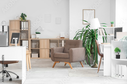 Interior of light office with desks, armchair and plants