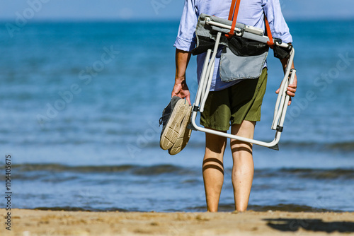 Illustration d'un homme portant ses chaussures et une chaise plainte au bord d'une plage a Hyeres (Var).